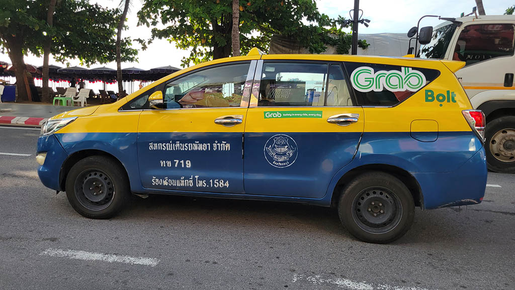 Blue and yellow Pattaya taxi parked roadside displaying Grab and Bolt decals, illustrating transport options for getting to Pattaya and away again.